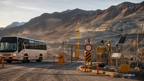 Acceso a una faena minera con barreras de control, un bus de personal, señalética de ingreso restringido y un panel de monitoreo geotécnico.