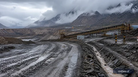 Acceso a una faena minera con lluvia reciente, canaletas de drenaje, señalética de seguridad y equipos detenidos por el temporal.
