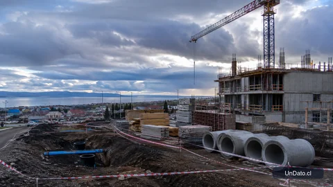 Obra habitacional en Punta Arenas con grúa, materiales de construcción y trabajos de urbanización en un entorno austral.