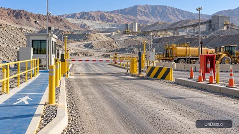 Acceso señalizado a una faena minera con rutas demarcadas, barrera de ingreso y maquinaria en un área delimitada.
