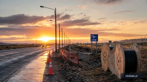 Ruta vial en Magallanes con postes de iluminación instalados, conos de seguridad, barreras de obra y señalización hacia el aeropuerto.