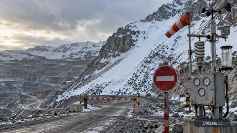 Acceso restringido a un rajo minero cordillerano junto a un panel meteorológico y una ruta señalizada.