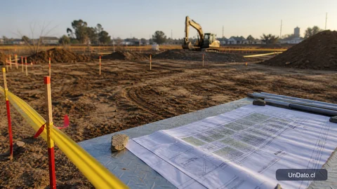 Terreno de obra con estacas topográficas, cinta de seguridad, tierra removida y planos de urbanización para un proyecto habitacional.