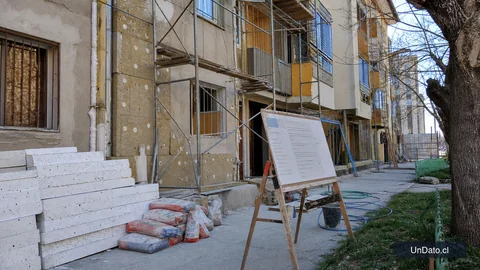 Fachada en reparación con andamios livianos, paneles aislantes y señalética de un llamado DS27 en un barrio urbano.